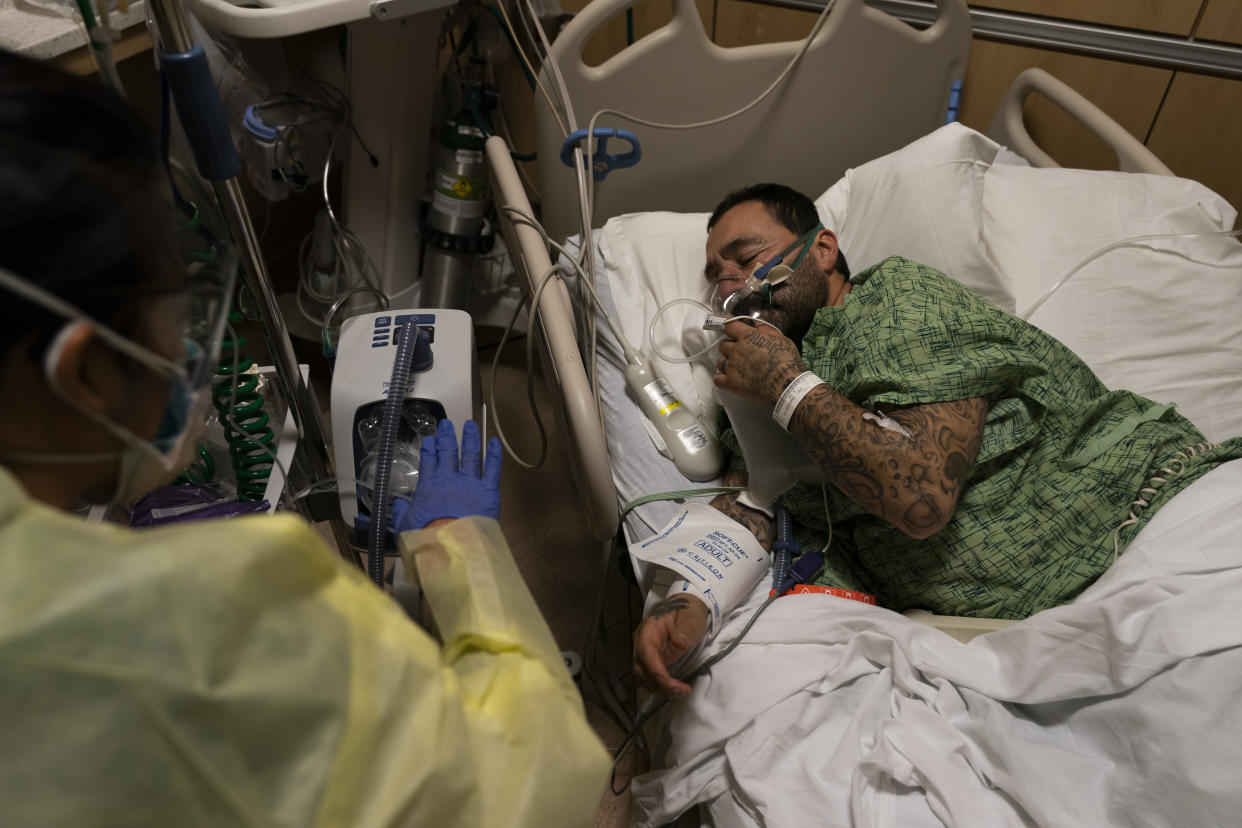 Registered nurse Emily Yu gestures to Paul Altamirano, 50, while treating him in a COVID-19 unit at Providence Holy Cross Medical Center in Los Angeles, Monday, Dec. 13, 2021. "This is nowhere to be. I didn't take it. Now I'm regretting it," said the unvaccinated patient. "I hope I make it. I just gotta be strong." (AP Photo/Jae C. Hong)