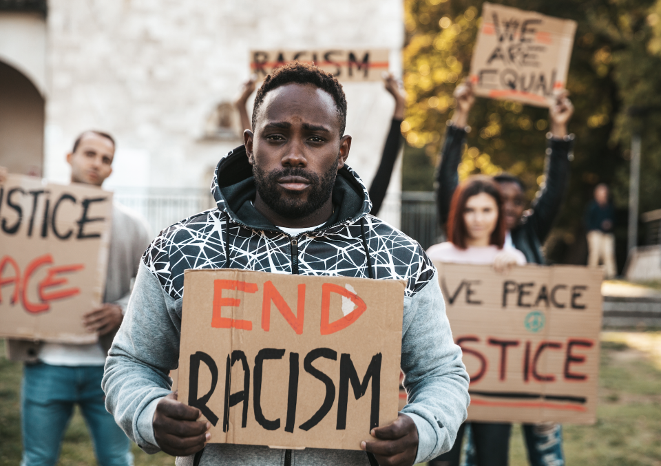A group of protestors, led by a man holding a sign that reads "End Racism," marches holding signs with messages advocating for justice and equality