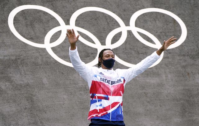 Kye Whyte, wearing a face mask, raises both his arms to celebrate winning a silver medal on the podium in Tokyo