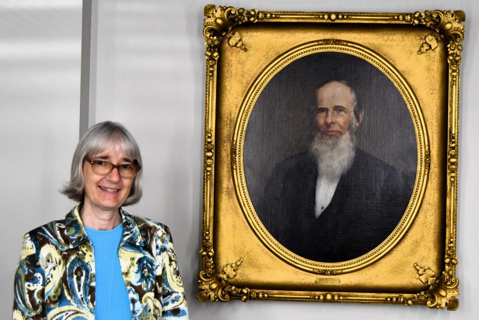 Pam Hoesman stands next to the portrait of Sardis Birchard founder of the library.