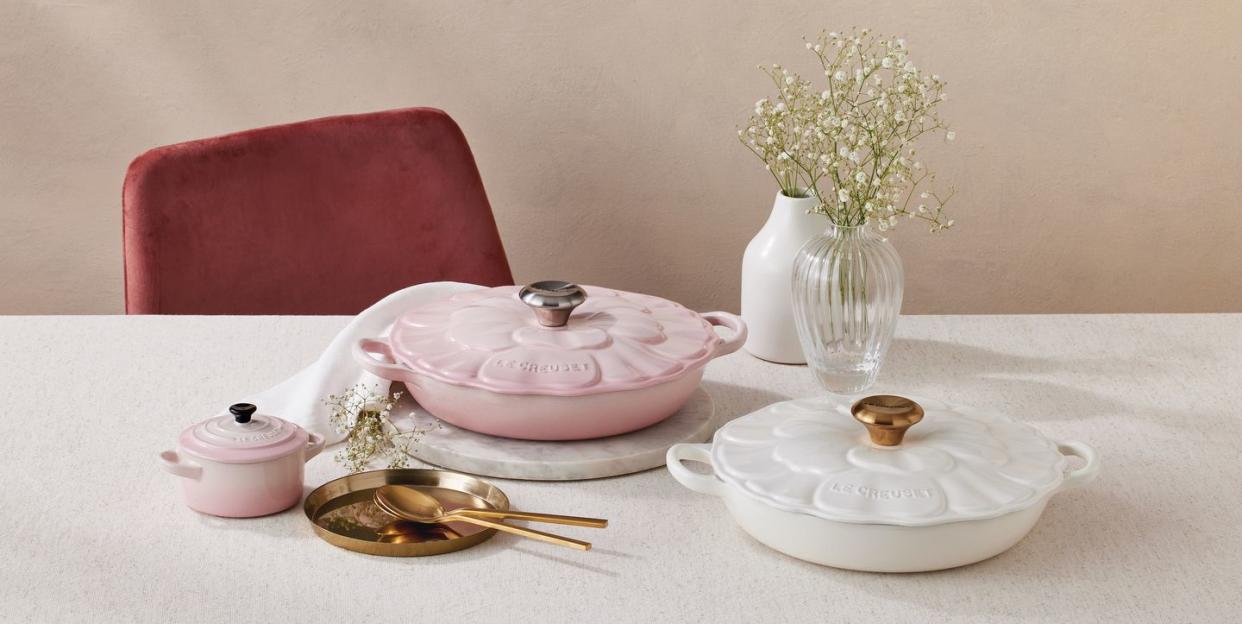 a table with a plate and a vase with flowers on it and the new le creuset floral casserole dish