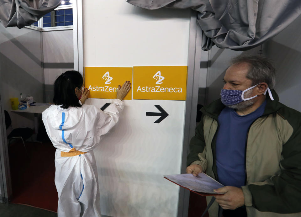 In this photo taken Sunday, March 21, 2021, a medical worker wearing protective gear sets up boards with the names of the vaccines at a vaccination center in Belgrade, Serbia. The Serbian police brought for questioning on Thursday a known Serbian doctor and some other vocal anti-vaccination activists, saying they are jeopardizing the Balkan country's so-far successful coronavirus inoculation drive. (AP Photo/Darko Vojinovic)