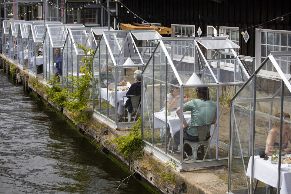 FILE - In this Monday, June 1, 2020 file photo, customers seated in small glasshouses enjoy lunch at the Mediamatic restaurant in Amsterdam, Netherlands. The coronavirus pandemic is gathering strength again in Europe and, with winter coming, its restaurant industry is struggling. The spring lockdowns were already devastating for many, and now a new set restrictions is dealing a second blow. Some governments have ordered restaurants closed; others have imposed restrictions curtailing how they operate. (AP Photo/Peter Dejong, File)
