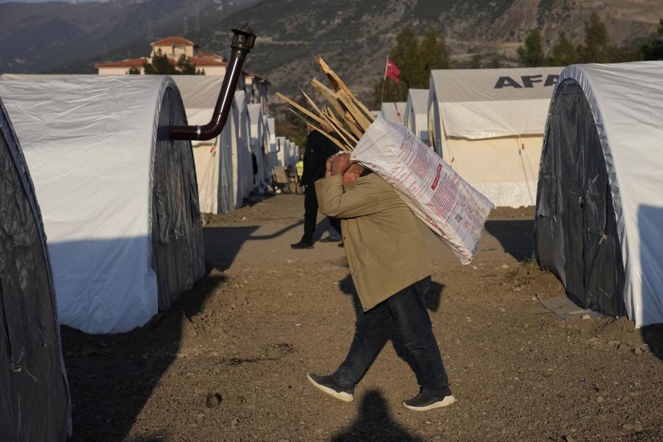 FILE - A Turkish man who lost his house in the devastating earthquake, carries wood at a makeshift camp, in Iskenderun city, southern Turkey, on Feb. 14, 2023.. Hundreds of thousands of people are seeking shelter after the Feb. 6 earthquake in southern Turkey left homes unlivable. Many survivors have been unable to find tents or containers dispatched to the region by the government and aid agencies, Instead they have sought refuge in any structure that can protect them from the winter conditions, including greenhouses, rail carriages and factories. (AP Photo/Hussein Malla)