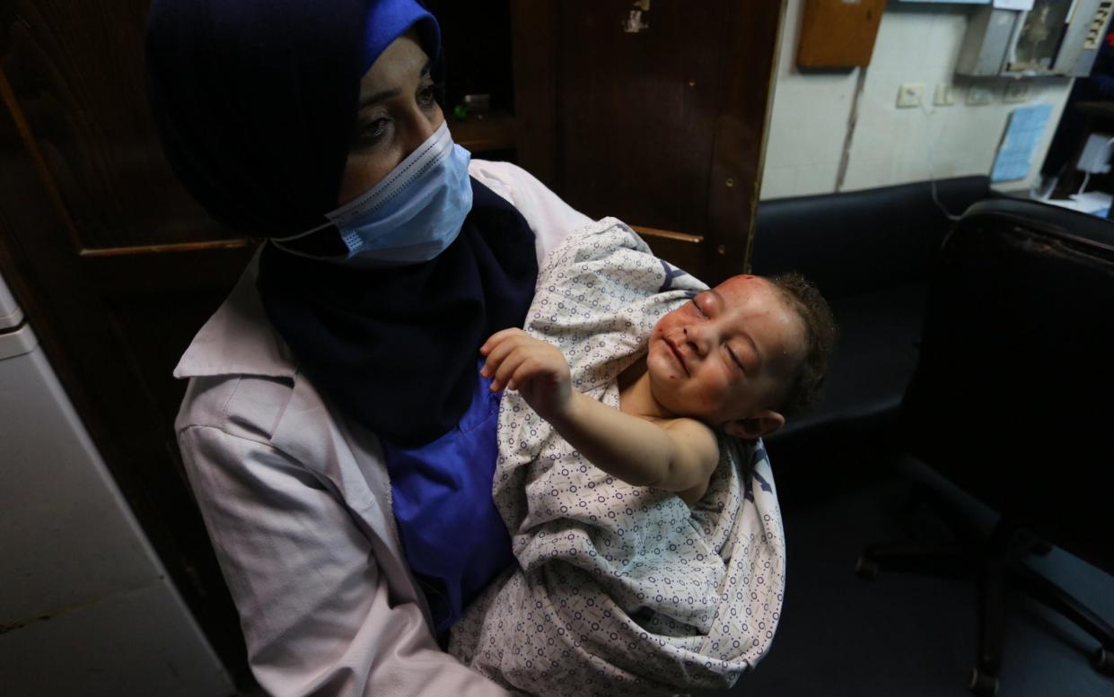 A nurse holds a baby, who was pulled alive from under the rubble while seven other family members perished, at Al-Shifa Hospital, Gaza, - APAImages/Shutterstock 