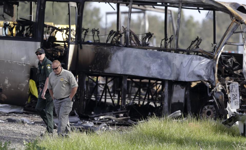 Glenn County Sheriff's officers walk past the remains of a tour bus that was struck by a FedEx truck on Interstate 5 Thursday in Orland, Calif., Friday, April 11, 2014. At least ten people were killed and dozens injured in the fiery crash between the truck and a bus carrying high school students on a visit to a Northern California College. (AP Photo/Jeff Chiu)