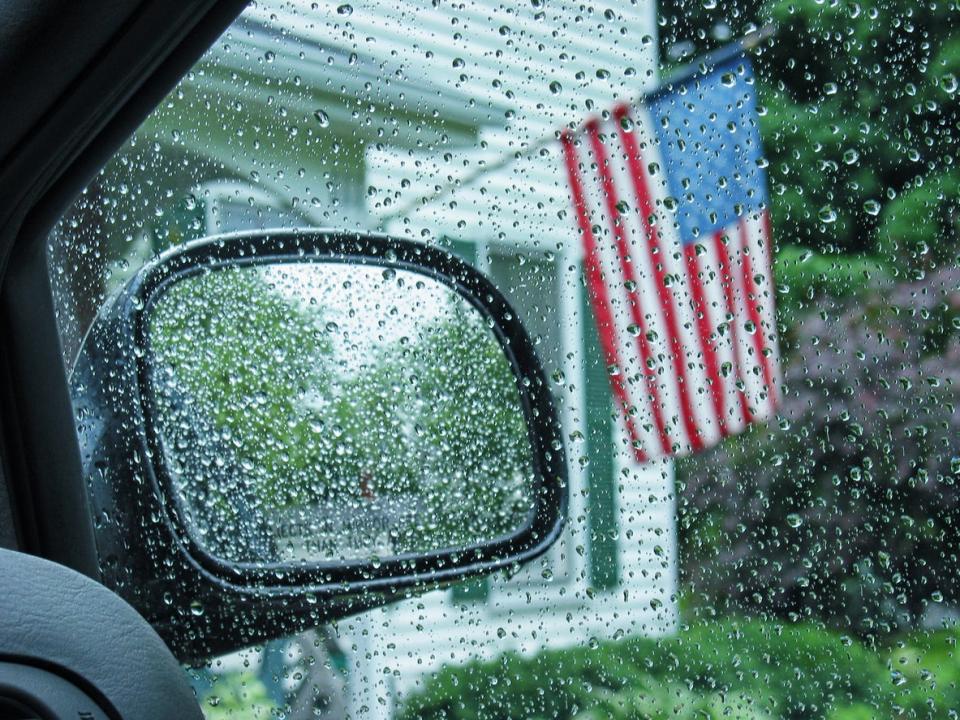 view from inside a car of an American flag hanging from a house in the rain