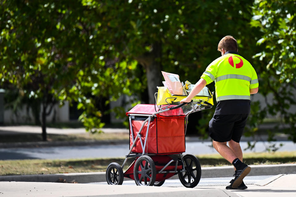 An Australia Post worker walks along the street with a mail trolley.