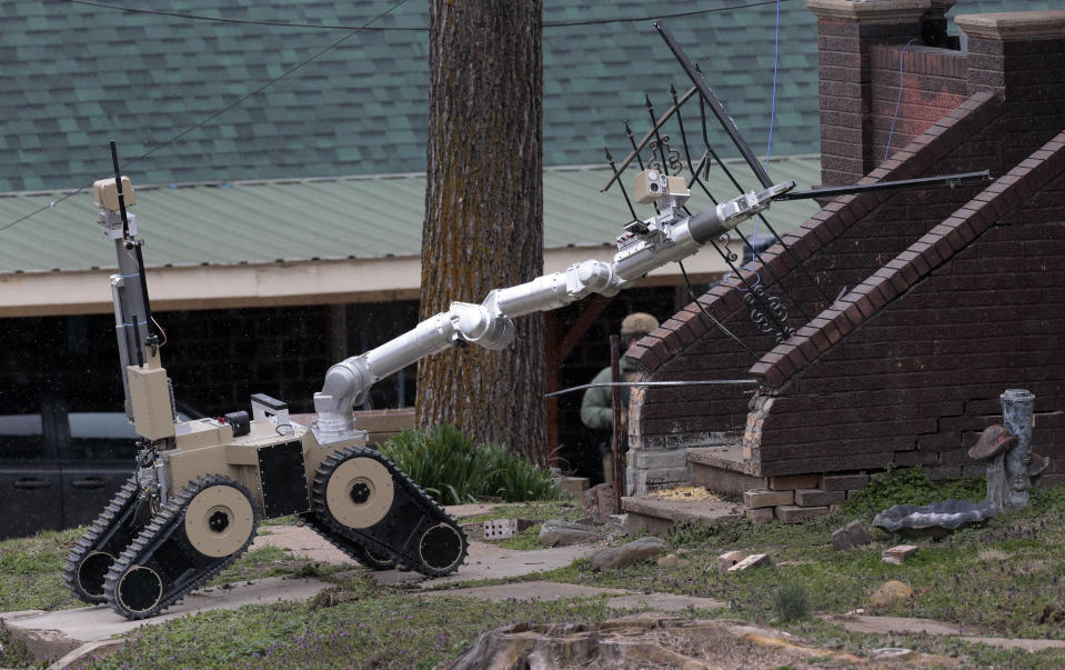 A robot removes the storm door of a home as tactical units from the Missouri Highway Patrol and St. Charles County police wait outside to search for a man accused of shooting two Hermann police officers Sunday night, on Monday, March 13, 2023, in Hermann, Mo. The St. Louis Post-Dispatch reported that police are focusing their search for a suspect Kenneth Lee Simpson on a home along Highway 19 near Hermann, not far from where the shooting happened. (Robert Cohen/St. Louis Post-Dispatch via AP)