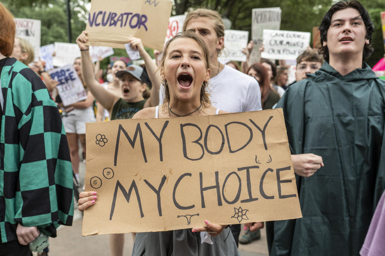 A young woman holds a hand-inked placard saying: My Body, My Choice, in a group of protesters shouting and holding similar placards.