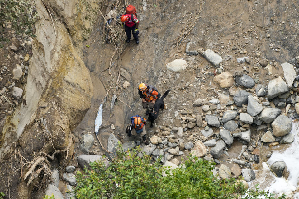 Firefighters and a search dog look for survivors after homes of the "Dios es fiel," or God is Loyal shanty town were swept away overnight by a swollen Naranjo River, on the outskirts of Guatemala City, Monday, Sept. 25, 2023. (AP Photo/Moises Castillo)