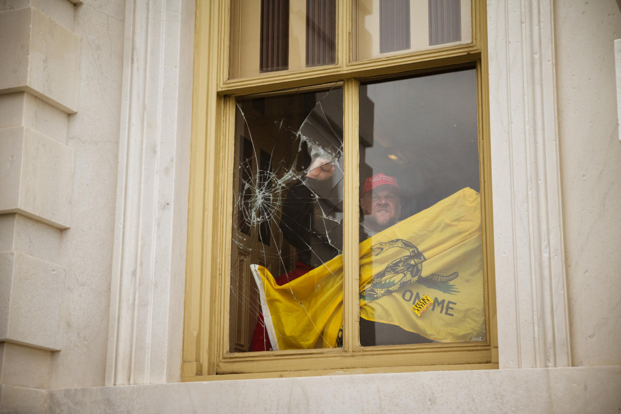 A member of a pro-Trump mob shatters a window with his fist from inside the Capitol