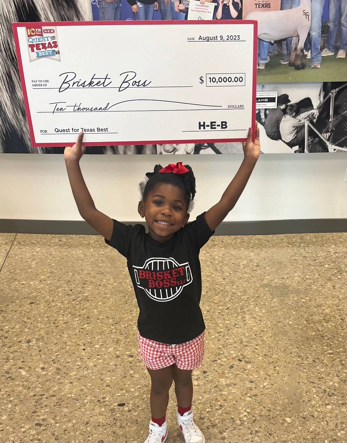 Royce Simmons’ granddaughter holds a $10,000 Brisket Boss prize check from H-E-B.