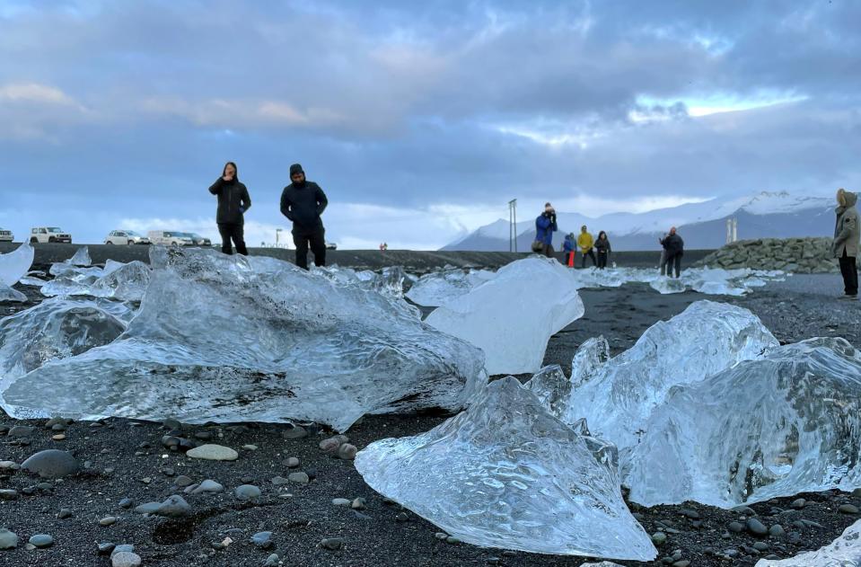 This Nov. 18, 2023 image provided by Beth Harpaz shows visitors amid mini-icebergs on Diamond Beach on Iceland's South Coast ((Beth Harpaz via AP))