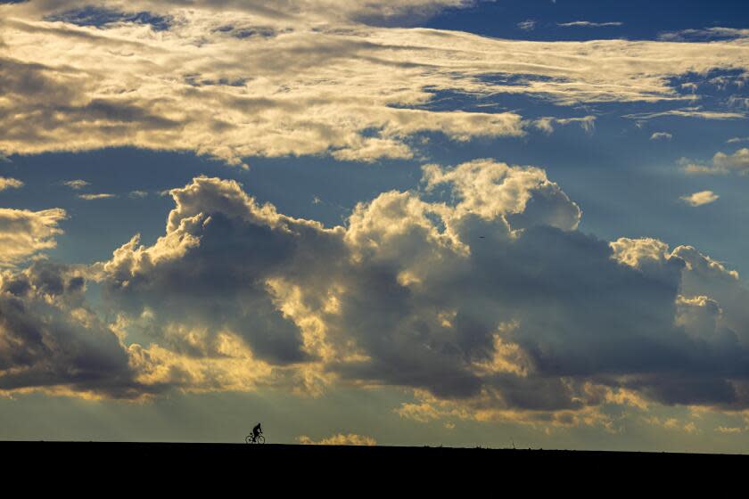 IRWINDALE, CA - AUGUST 16: A lone cyclist dwarfed by monsoon clouds rising above Santa Fe Dam in on a hot and muggy day Irwindale, CA. (Irfan Khan / Los Angeles Times)