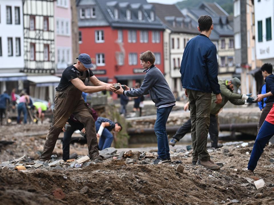 A man hands a piece of ruble to a young boy as citizens clean up the flood damage. A