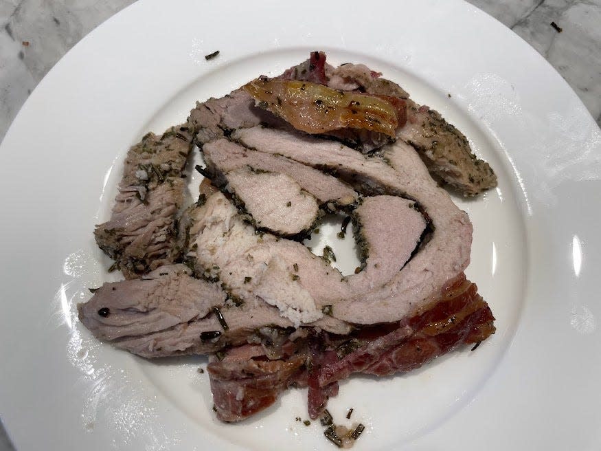 Sliced pork and bacon on a white plate on a gray counter