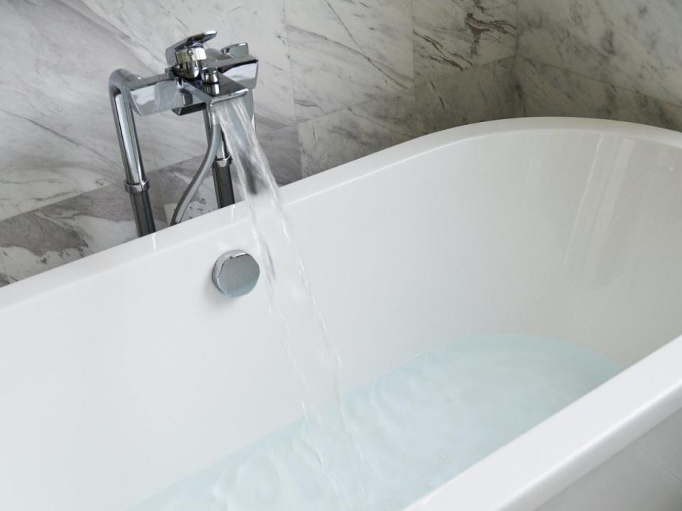 Water running from faucet in a modern bathtub with some water in tub basin.