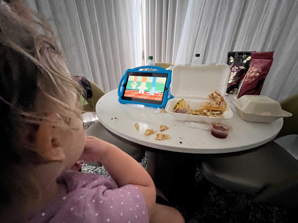 A child watching an iPad on a table while eating takeout food.