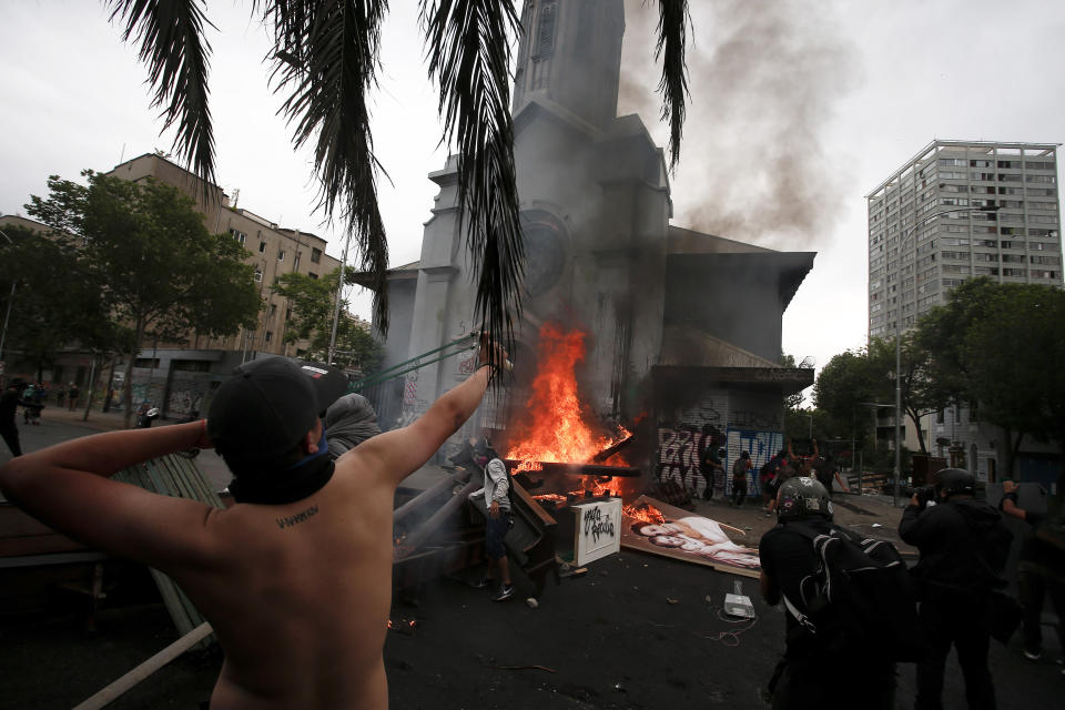 An anti-government protester aims his sling shot at a church after it was looted, in Santiago, Chile, Friday, Nov. 8, 2019. Chile's president on Thursday announced measures to increase security and toughen sanctions for vandalism following three weeks of protests that have left at least 20 dead. (AP Photo/Luis Hidalgo)