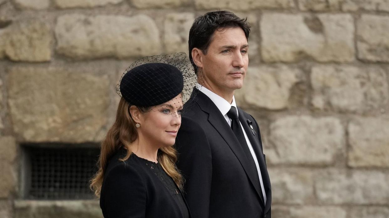 sophie grégoire trudeau and justin trudeau stand next to each other, they wear black formal clothes and have solemn expressions on their faces