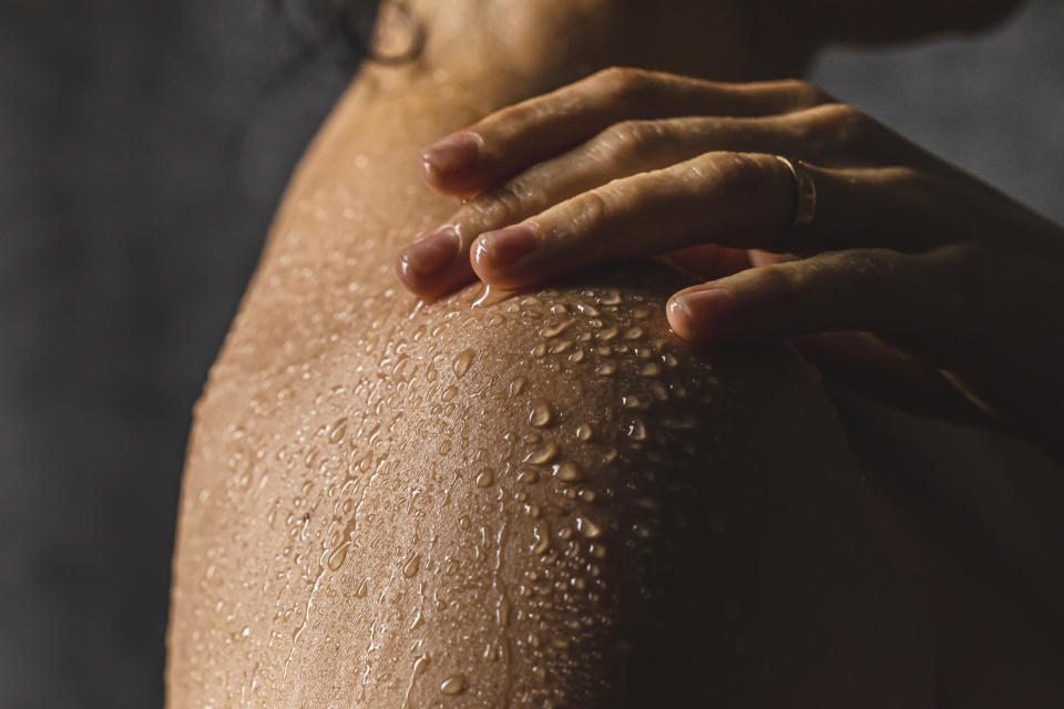 A close-up of a person's shoulder with water droplets on their skin, and their hand resting on it. The image conveys a sense of freshness and moisture