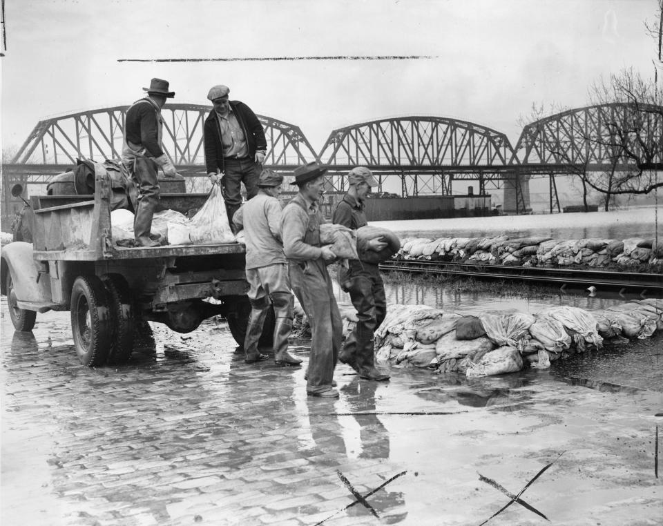 Photo by Art Abfier, March 5, 1945. Employees of the city reinforce a sandbag levee east of Campbell St. THe sandbags are delivered holding the Ohio River away from the Point just by trucks. The Big Four Bridge is in the background.