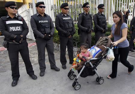 A woman and her child walks past policemen standing guard as anti-coup protesters gather outside the Australian embassy in Bangkok in this June 4, 2014 file photo. REUTERS/Chaiwat Subprasom/Files