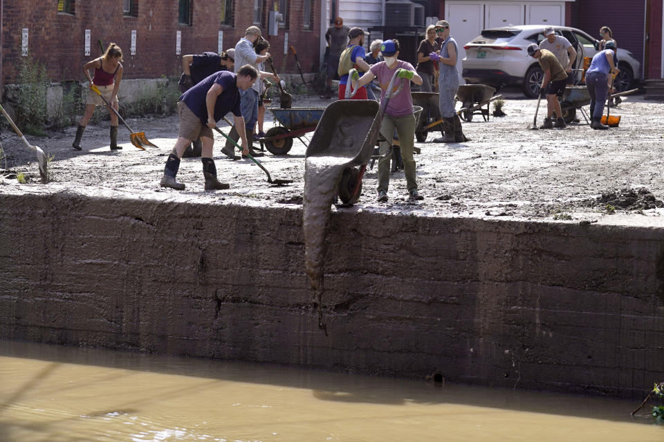 Volunteers clean up a downtown parking area on the banks of the Winooski River, Wednesday, July 12, 2023, in Montpelier, Vt. Following a storm that dumped nearly two months of rain in two days, Vermonters are cleaning up from the deluge of water. (AP Photo/Charles Krupa)