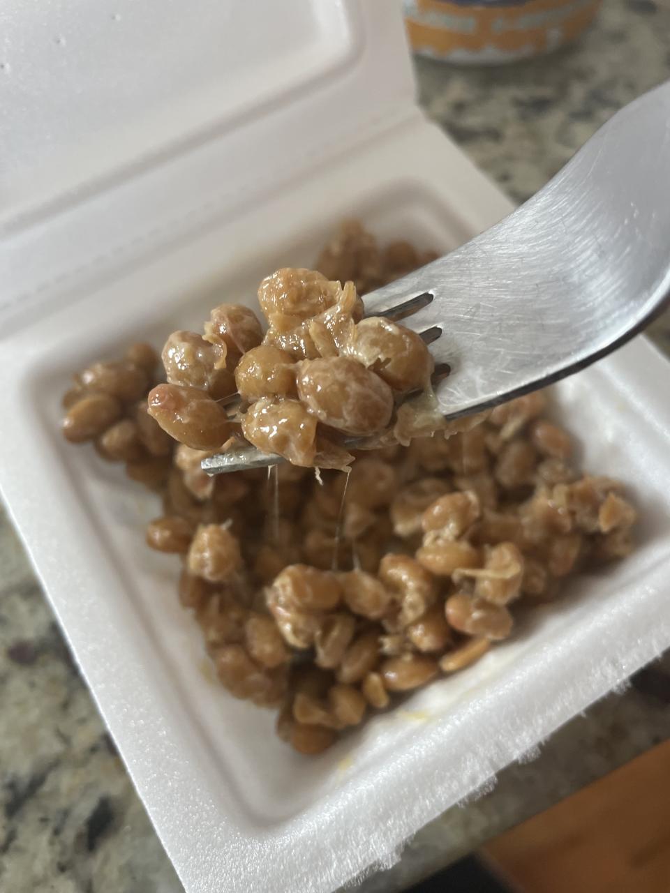 A fork is lifting natto (fermented soybeans) from a styrofoam container