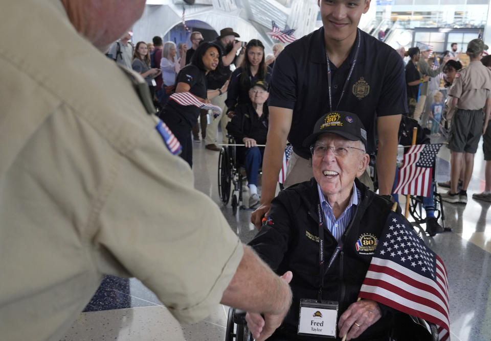 Fred Taylor, bottom right, a World War II veteran fighter pilot, shakes hands with Chet Reeder, as Howard Lin helps Taylor along before boarding a plane with others at Dallas Fort Worth International Airport in Dallas Friday, May 31, 2024. A group of World War II veterans are being flown from Texas to France where they will take part in ceremonies marking the 80th anniversary of D-Day. (AP Photo/LM Otero)