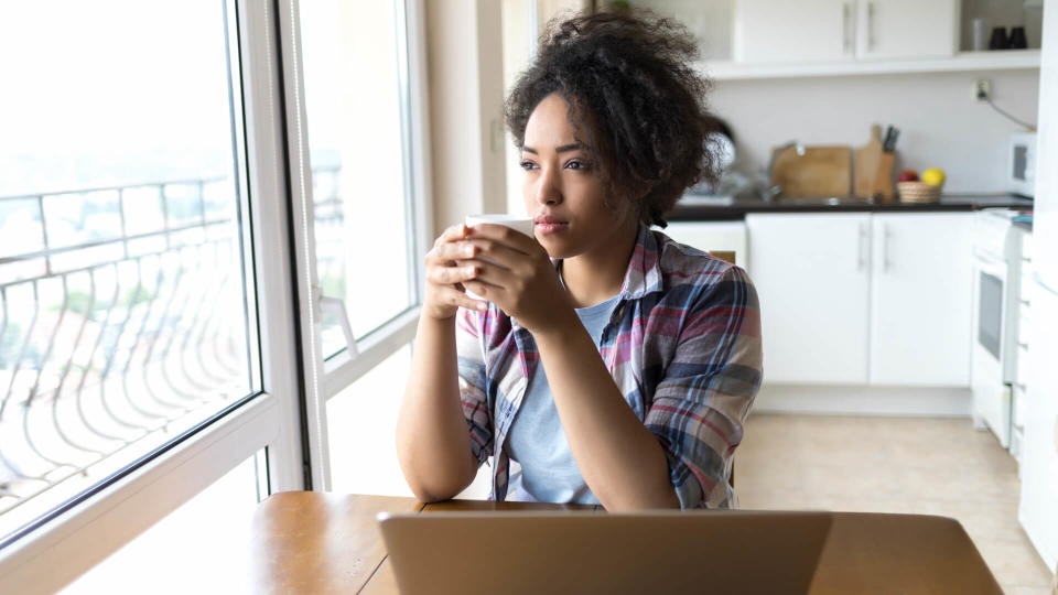 Woman drinking coffee and using laptop at home.