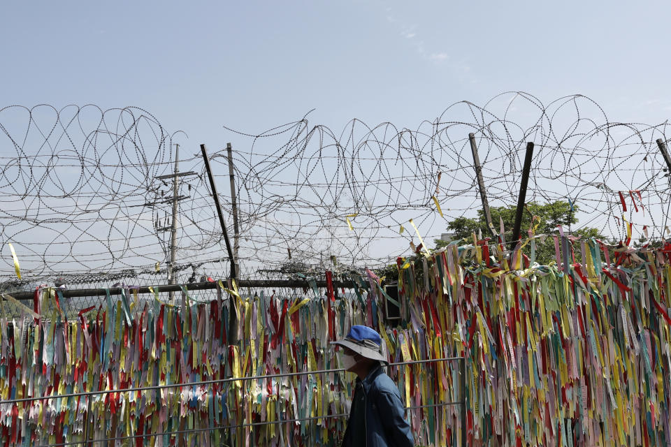A visitor wearing a face mask walks in front of the wire fence decorated with ribbons written with messages wishing for the reunification of the two Koreas at the Imjingak Pavilion in Paju, South Korea, Sunday, June 14, 2020. South Korea on Sunday convened an emergency security meeting and urged North Korea to uphold reconciliation agreements, hours after the North threatened to demolish a liaison office and take military action against its rival. (AP Photo/Lee Jin-man)