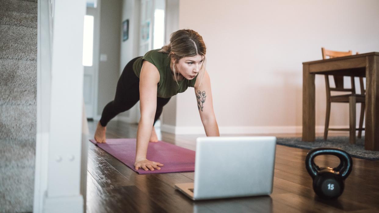 An adult woman does yoga and strength training exercises on a mat in her living room.