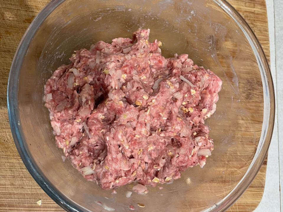 ground meat mixed with onion, spices, and oats in a glass mixing bowl on a wooden cutting board