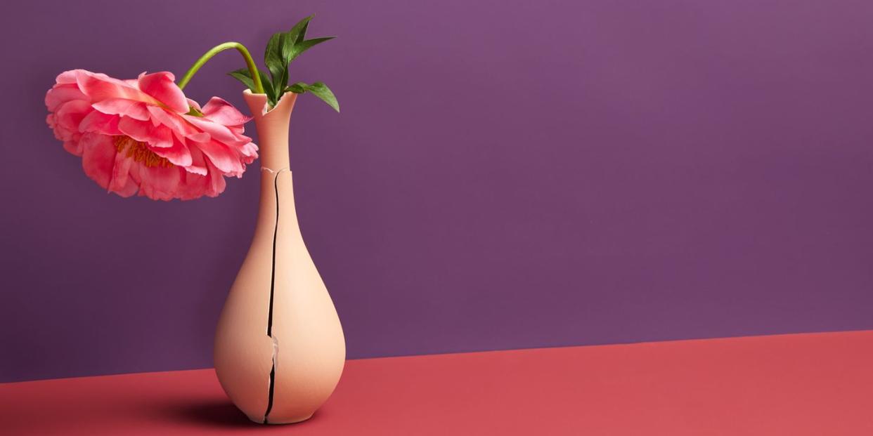 dying pink flower in cracked, ceramic vase