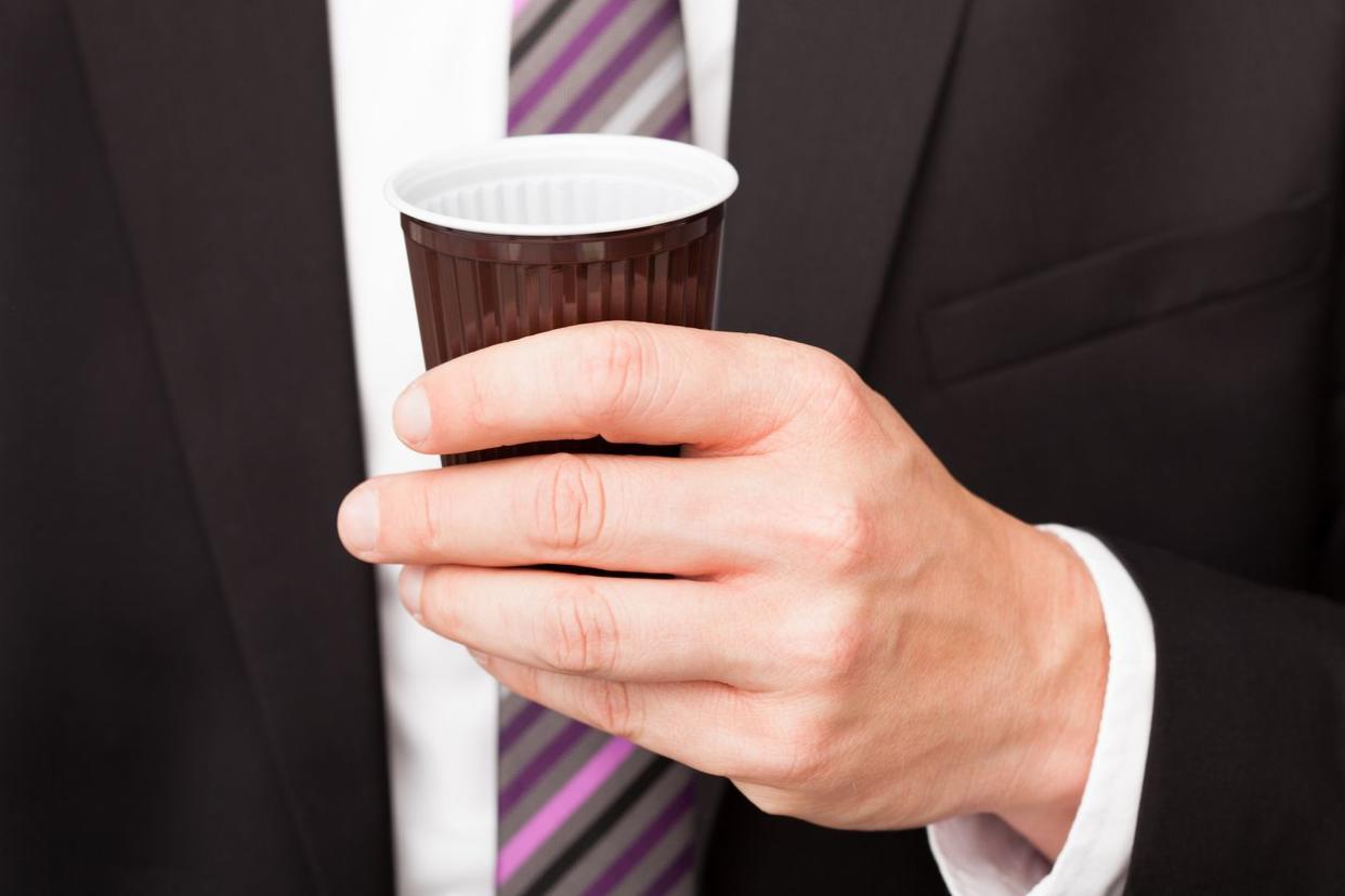 An employee holding a small cup of coffee.