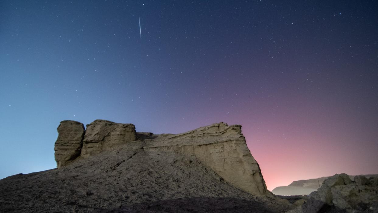  A streak of light crosses the night sky above the desert. 