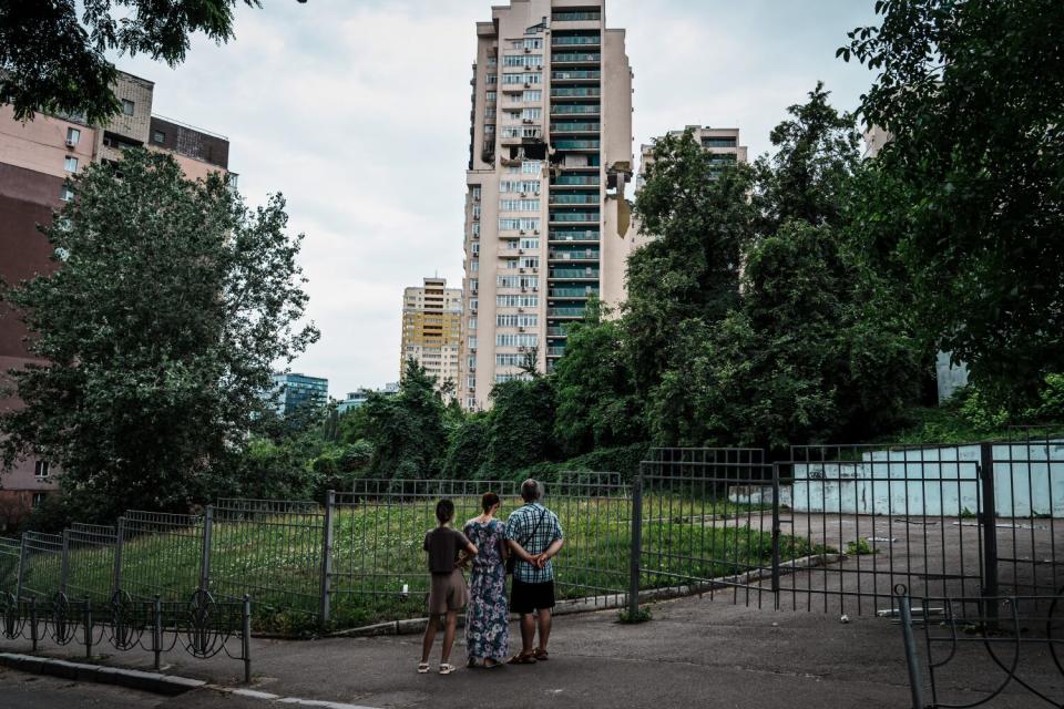 Residents look at an apartment building with black, gaping holes around the 18th floor