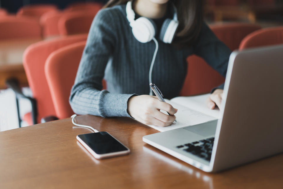 Beautiful smiling female student using online education service. Young woman looking in laptop display watching training course and listening it with headphones. Modern study technology concept