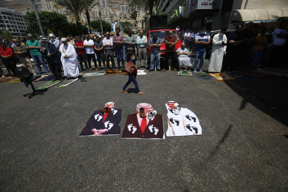 Palestinians perform Friday prayer before burning cutouts pictures of U.S. President Donald Trump, Abu Dhabi Crown Prince Mohammed bin Zayed al-Nahyan and and Israeli Prime Minister Benjamin Netanyahu during a protest against the United Arab Emirates' deal with Israel, in the West Bank city of Nablus, Friday, Aug. 14, 2020.(AP Photo/Majdi Mohammed)