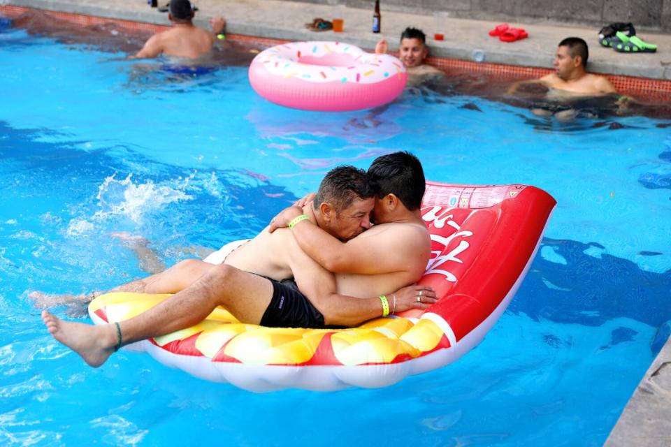 Two men embrace on a flotation device in a swimming pool.
