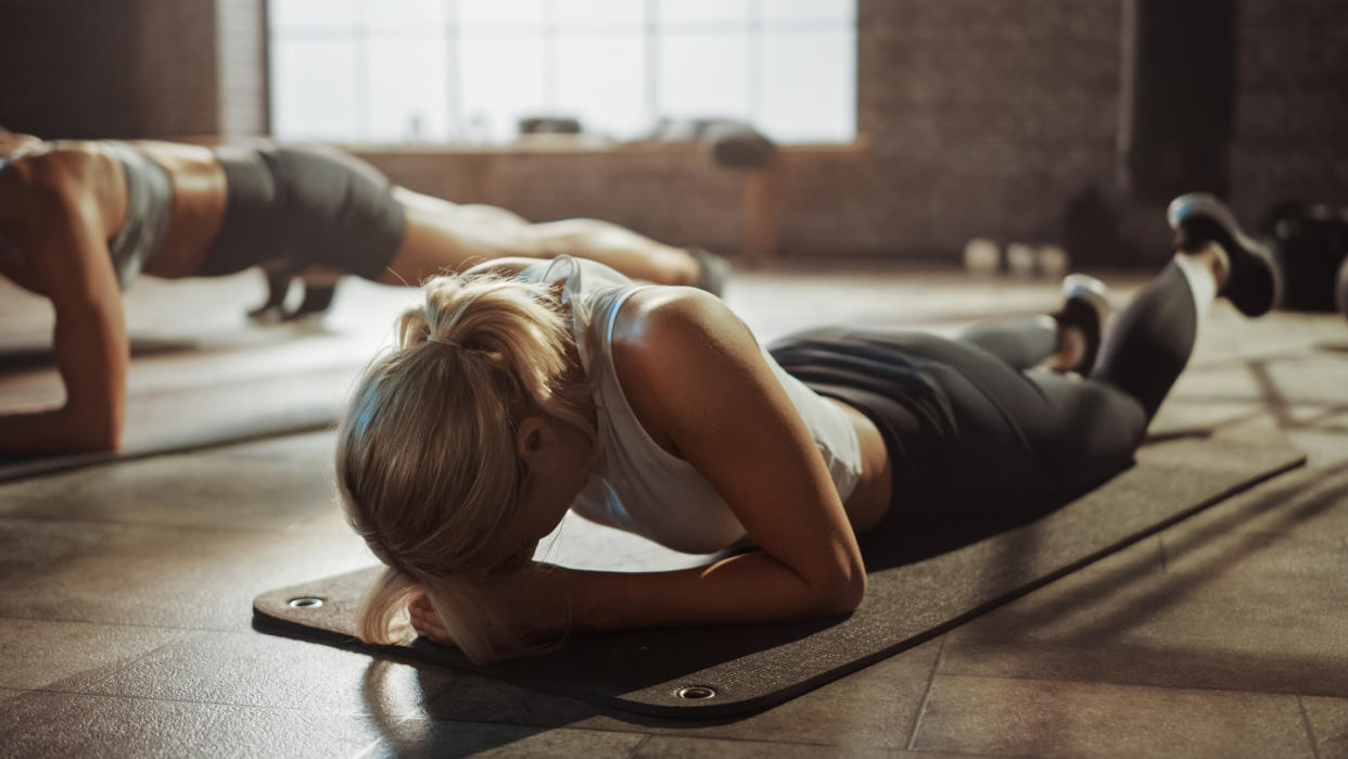  Woman lies face down on exercise mat looking exhausted 