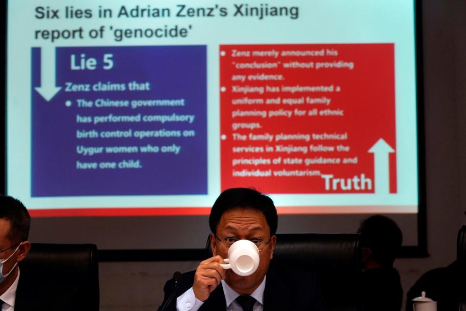 Xu Guixiang, a deputy spokesperson for the Xinjiang regional government, drinks from a cup near a slide refuting claims of genocide during a press conference in Beijing, China. - Ng Han Guan/AP Photo