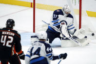 Winnipeg Jets goaltender Connor Hellebuyck, right, deflects a shot with Anaheim Ducks defenseman Josh Manson, left, and defenseman Josh Morrissey, center, watching during the third period of an NHL hockey game in Anaheim, Calif., Tuesday, Oct. 26, 2021. (AP Photo/Alex Gallardo)