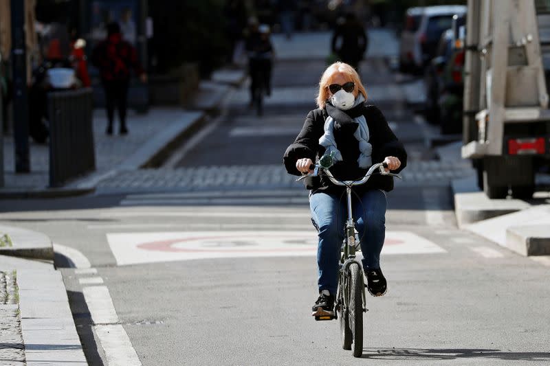 A woman wearing a protective face mask to prevent contracting the coronavirus rides her bicycle in Milan