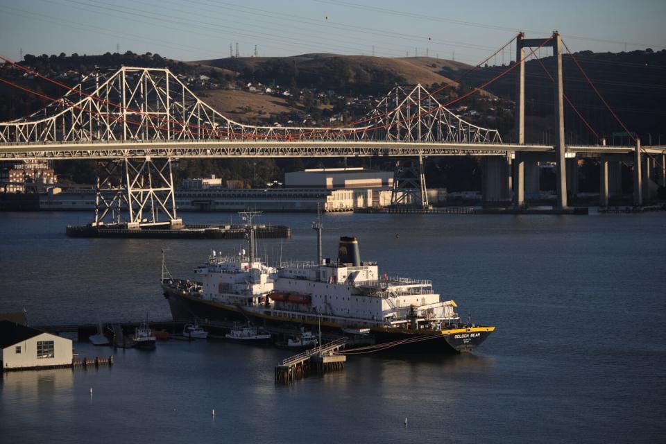 A 500-foot training ship with "Golden Bear" on its stern is framed on the water by a bridge and hills beyond it