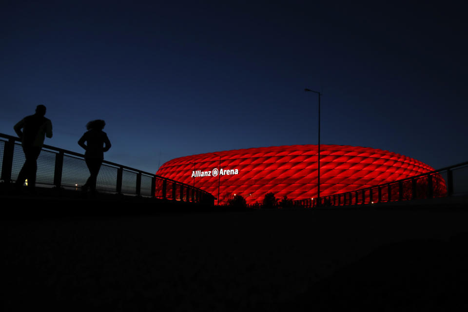 Jogger make their way after the sun sets at the 'Allianz Arena' soccer stadium in Munich, Germany, Monday, March 16, 2020. UEFA, are set to make a final decision when the UEFA executive committee meets on Tuesday March 17, 2020 after talks with clubs and leagues, about possibly delaying the Euro 2020 soccer tournament by a year as the continent grapples with the outbreak of the coronavirus. (AP Photo/Matthias Schrader)