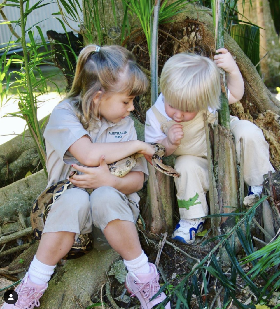 Robert Irwin and Bindi Irwin as children at Australia Zoo in Queensland, Bindi is holding a snake and showing Robert