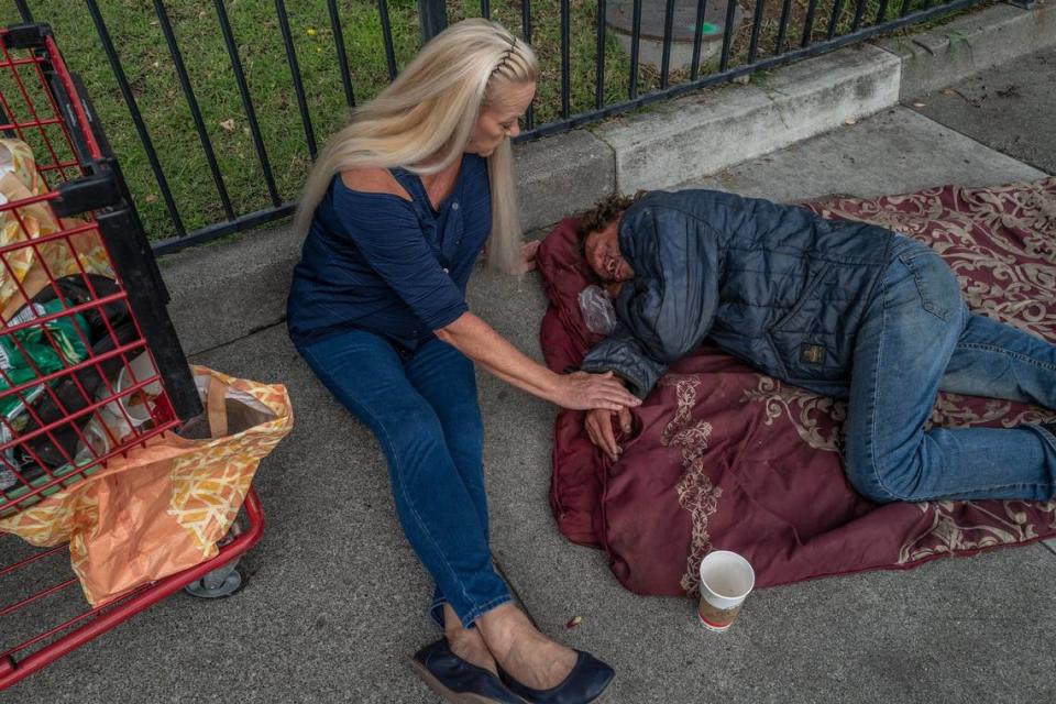 Linda Privatte, 65, caresses her brother Mark Rippee’s hand as she gently tries to wake him up on a sidewalk in Vacaville on Aug. 1. “Is it okay for me to clean your cart out for you so I can see what you need?” she asked.